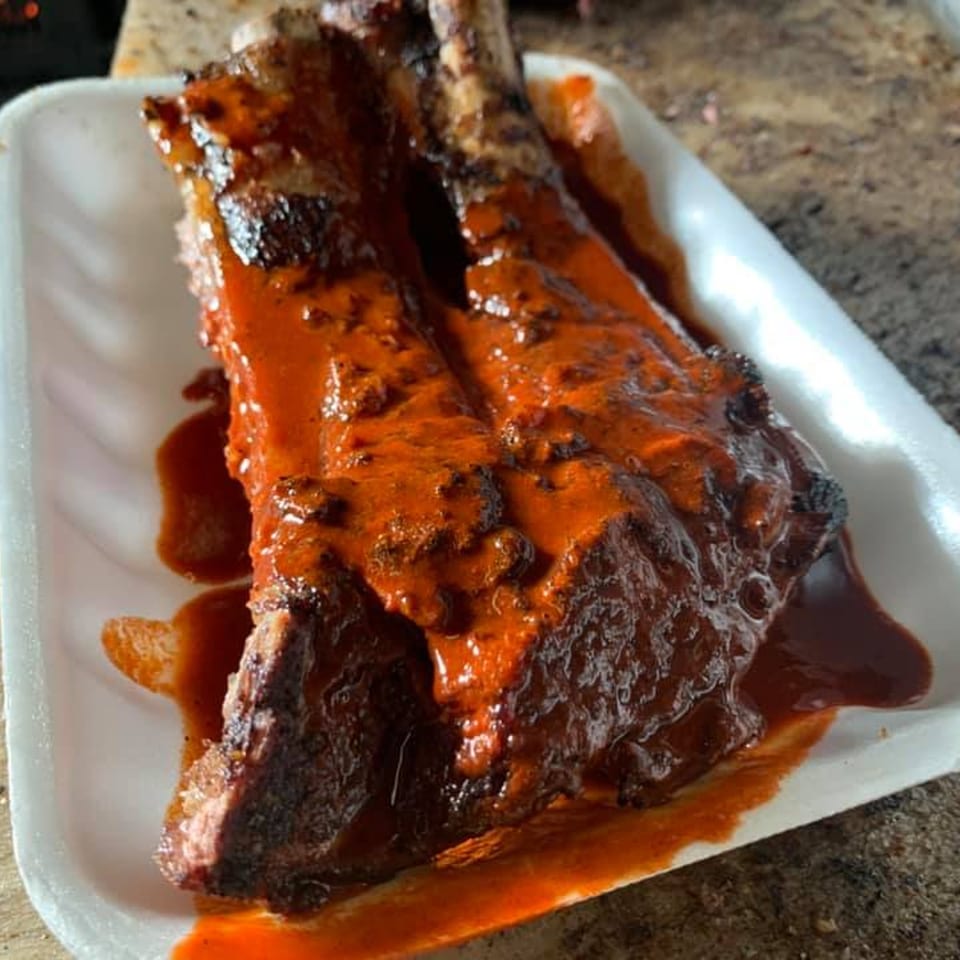 Two saucy barbecue ribs on a white styrofoam plate, glistening with red sauce.