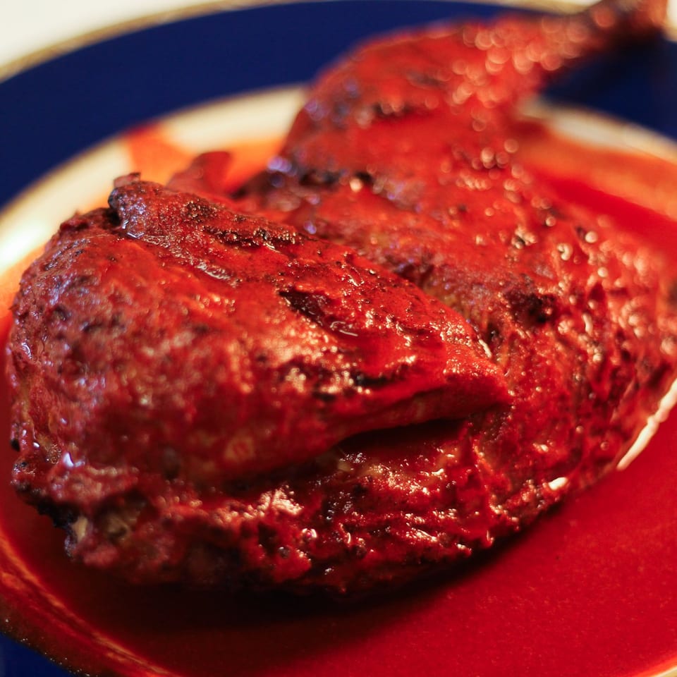 Close-up of a glistening, red barbecue chicken quarter on a plate with red sauce.