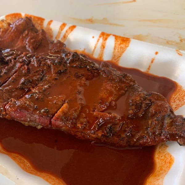 Close-up of a large piece of barbecue meat covered in rich red sauce on a white tray.