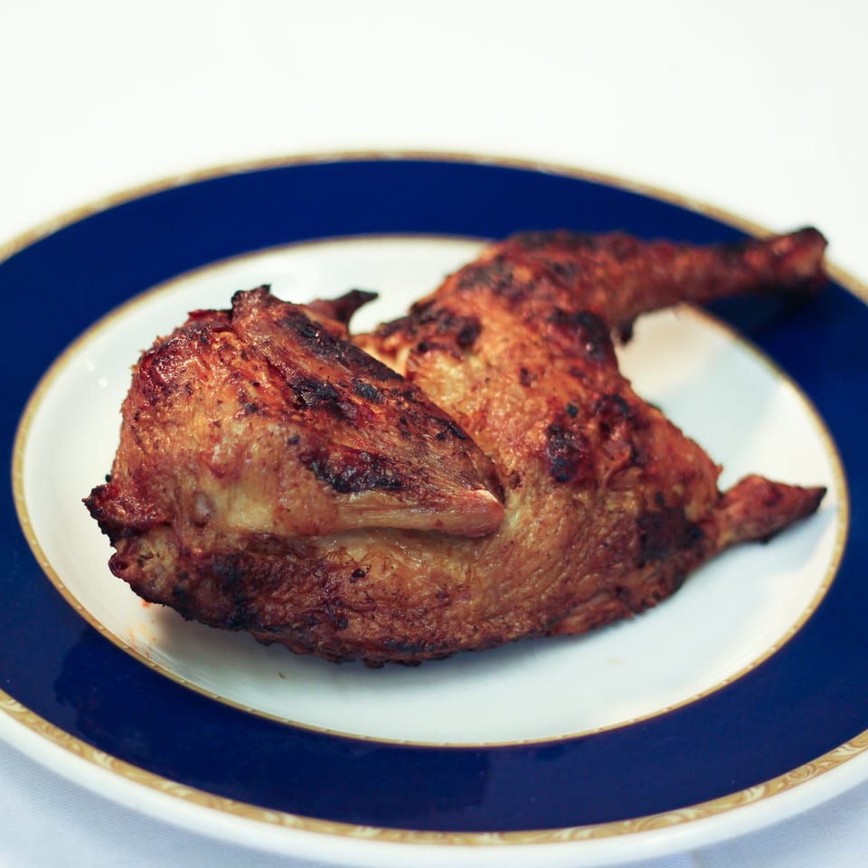 A golden-brown, grilled chicken quarter, likely from Parks Old Style Bar-B-Q, on a white plate with a blue and gold rim.